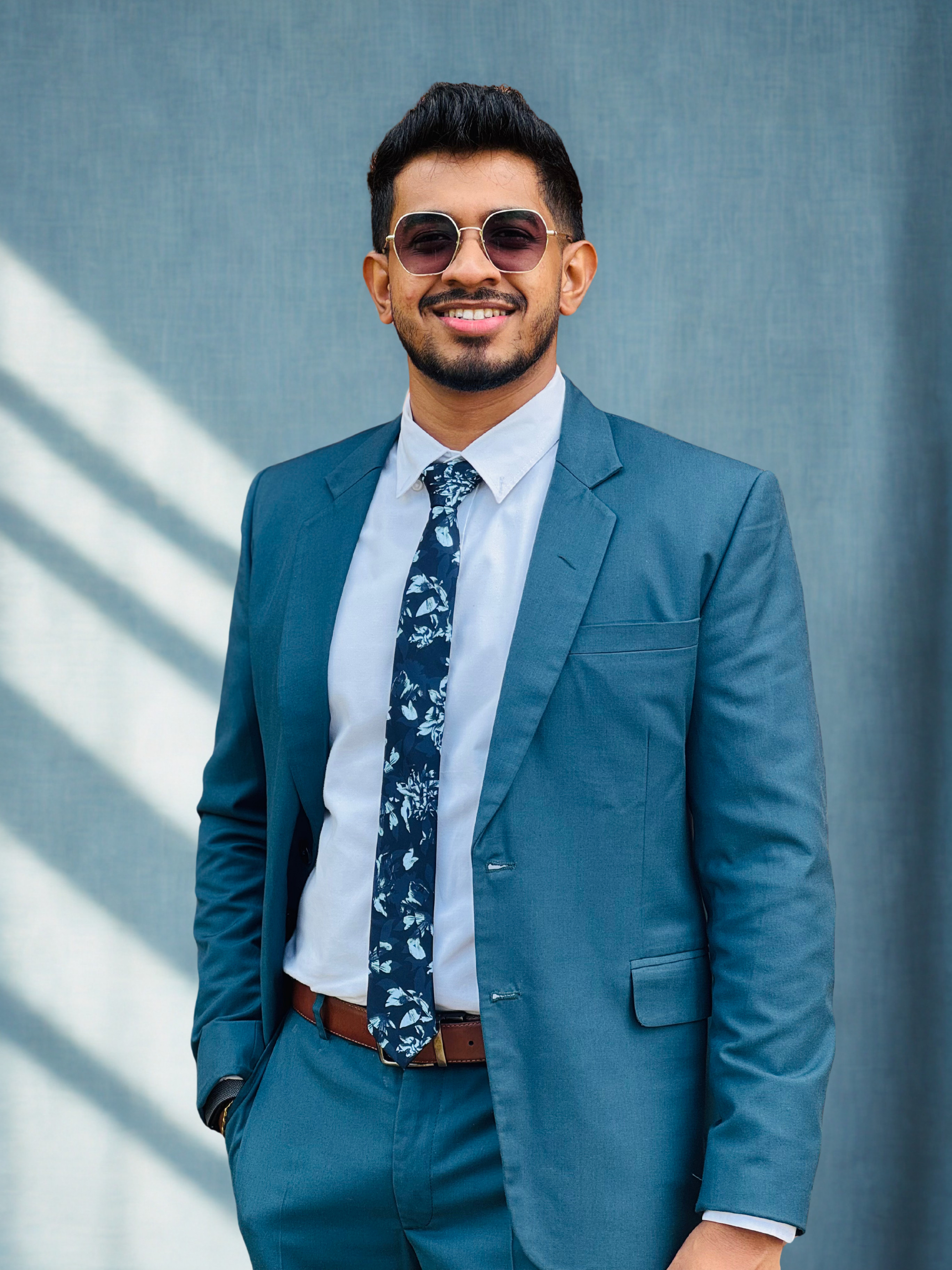 Kanishka Liyanage wearing a blue suit, patterned tie and sunglasses